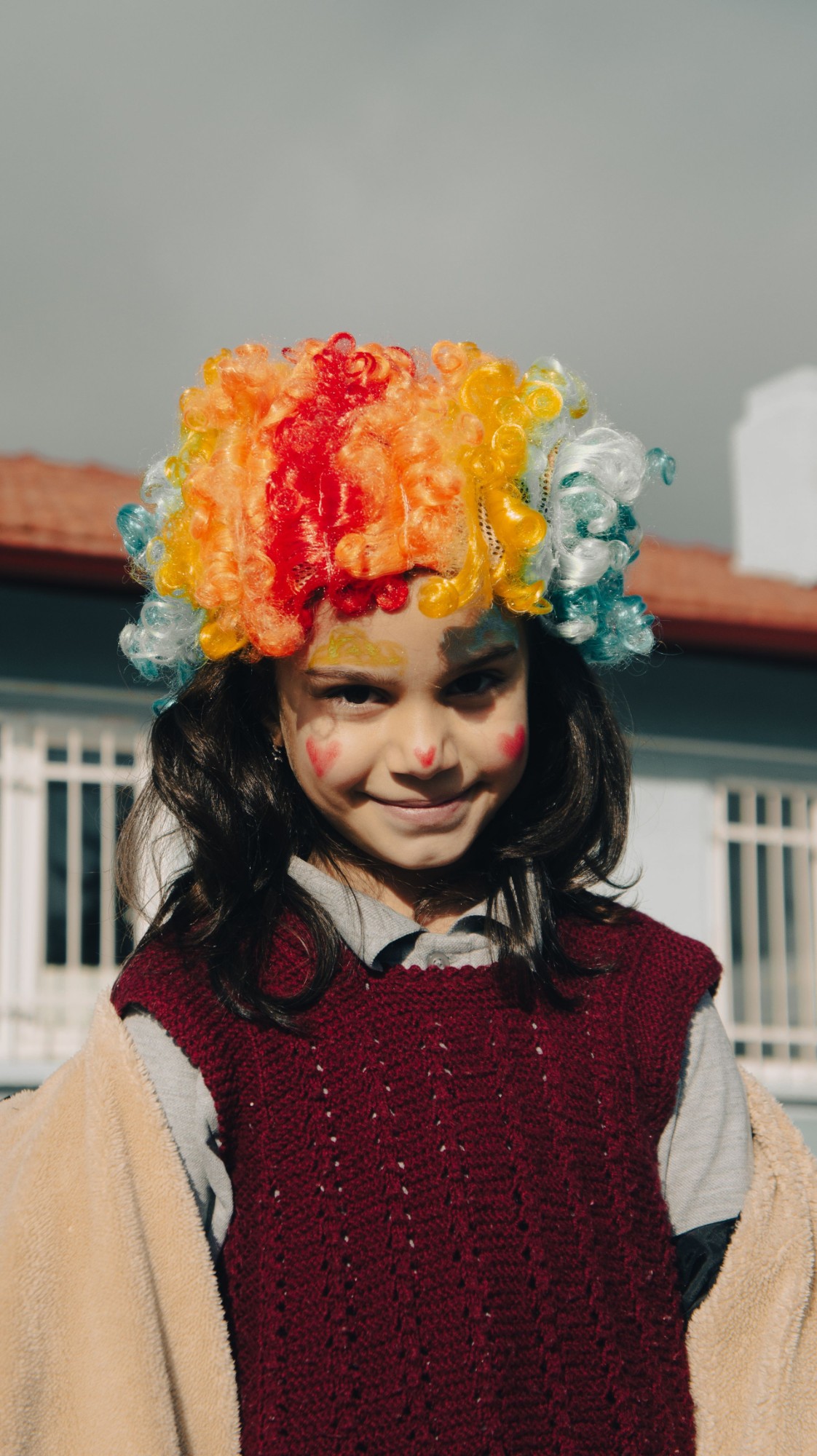 Criança vestida de palhaço, com peruca colorida e a cara pintada, numa brincadeira de Carnaval
